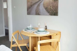 Uma sala de jantar com uma mesa de madeira, duas cadeiras e um quadro de uma estrada na parede.