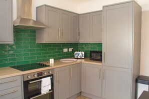 A kitchen with grey cabinets, a green tiled backsplash, a sink, a microwave, and an oven. - Cosy 3Bed Bungalow in West Kirby, Free Parking (West Kirby)