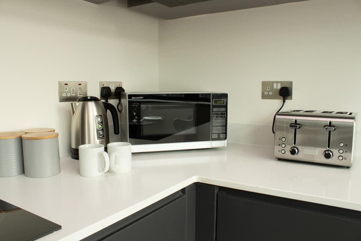 Una cocina con microondas, tostadora, hervidor y tazas sobre la encimera.