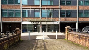 Un edificio de varios pisos con un letrero 'PARAGON', un acceso con portón y fachada de ladrillo.