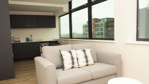 Una sala de estar moderna con un sofá, una mesita redonda y vistas de la ciudad a través de amplios ventanales.