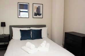 Una habitación de hotel con cama, almohadas, mesita de noche, lámpara y cómoda.