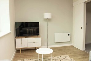 Una habitación con un televisor sobre un mueble de madera, una lámpara de pie blanca y un radiador blanco.