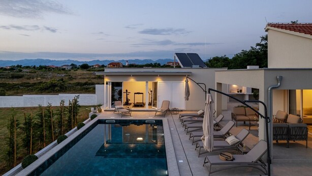 Ein modernes Haus mit Swimmingpool, Sitzgelegenheiten im Freien und Bergblick.