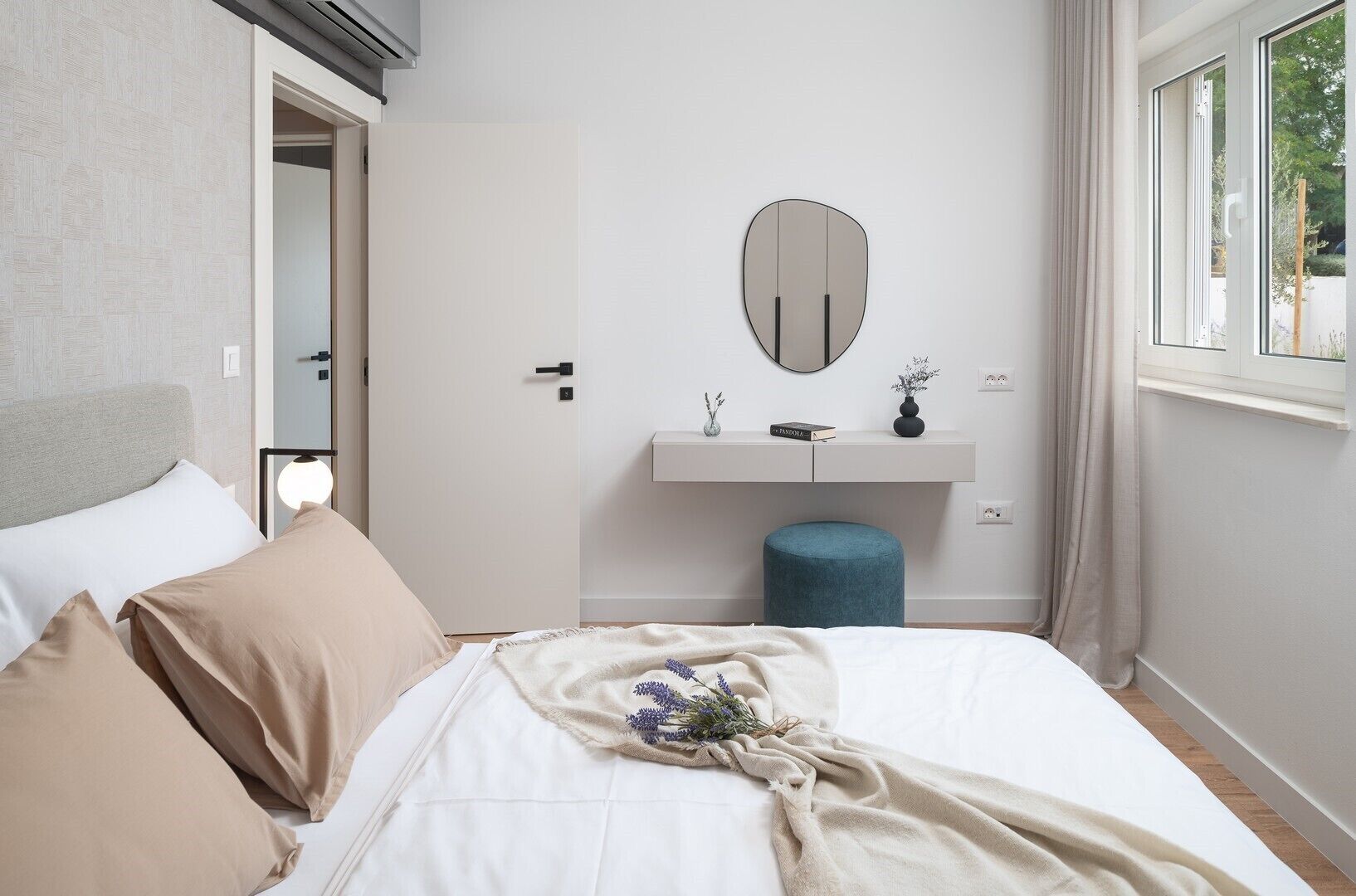 Een slaapkamer met een bed, nachtkastje, spiegel, raam en deur.