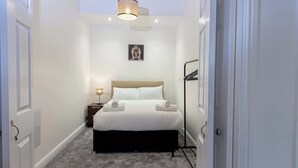 A hotel room with a bed, a bedside table, a lamp, a picture on the wall, and a ceiling light.