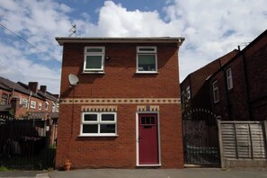 A two-story brick house with a red door, satellite dish, and a small garden. - Cosy & Fully Equipped Cottage in Swinton (Manchester)