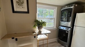 Une cuisine compacte dotée d’un four encastré, d’un réfrigérateur, d’une fenêtre offrant une belle vue, d’une estampe botanique encadrée et d’une petite table agrémentée d’une plante.