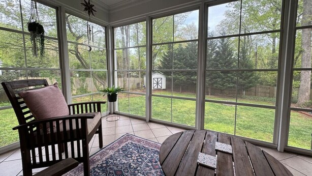 Une terrasse couverte avec un banc en bois, une table et une vue sur une cour verdoyante, visible à travers de grandes fenêtres.