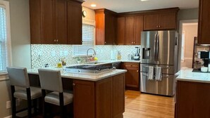 Une cuisine moderne avec des meubles en bois, un réfrigérateur en acier inoxydable et un îlot central doté de chaises.