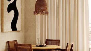 Un coin repas comprenant une table ronde en bois, six chaises en bois, un luminaire suspendu en fibres tressées et un grand tableau abstrait accroché au mur.