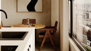 A modern kitchen with a built-in stove, a dining area with a round table and wooden chairs, a hanging light fixture, and a large window with a city view. - Kyoto Suites - Sleep inn Antwerp (Antwerp)