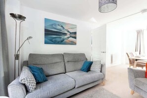 A modern living room with a grey sofa, a floor lamp, and a painting of a mountain landscape.
