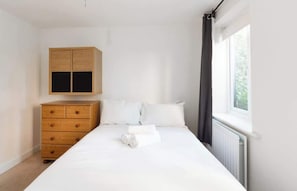 A bedroom with a bed, a wooden dresser, a wardrobe, and a window with curtains.