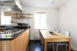 A compact kitchen with a stove, microwave, and wooden shelves.
