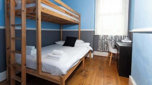 Habitación con literas, escritorio, silla, ventana con cortinas y radiador.