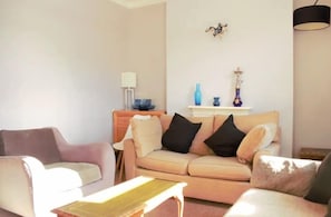 Een woonkamer met een beige bank, een kleintje tafel en een lamp.