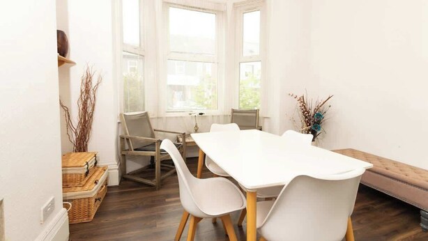Un comedor con una mesa blanca, cuatro sillas, un banco y vistas amplias a través de grandes ventanales.