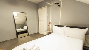 Una habitación de hotel con una cama, un espejo, una puerta y una mesita con una lámpara.