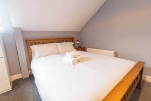 Un dormitorio con cama de madera, ropa de cama blanca, una mesita de noche con lámpara y un radiador.