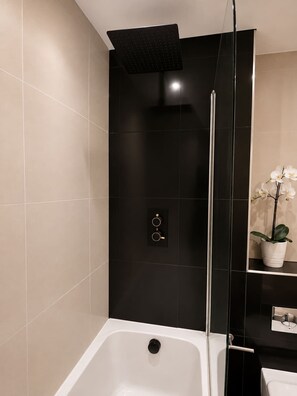 A modern bathroom with a bathtub, a showerhead, and a potted orchid.