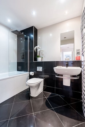 A modern bathroom with a glass-enclosed shower, a white toilet, a black sink, and a mirror.