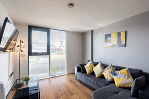 Uma sala de estar moderna com um sofá, uma televisão de tela plana, um luminário de teto e uma janela grande com persianas.
