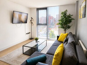 Een moderne woonkamer met een bank, een salontafel, een televisie en een groot raam met zonwering.