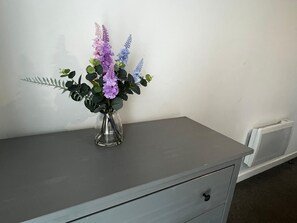 Een grijze ladekast met een glazen vaas gevuld met paarse en blauwe bloemen.