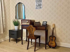 Una stanza con una scrivania in legno, una sedia, una chitarra, una radio e uno specchio.