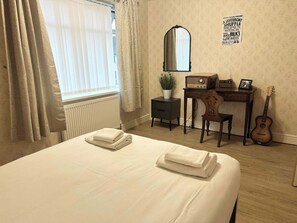 Una camera d'albergo con un letto, una scrivania, una sedia, una chitarra, uno specchio e un poster appeso al muro.