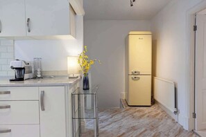 A kitchen with a white refrigerator, a coffee maker, and a vase with yellow flowers. - Cosy 2 Bed Apartment - Close to Leeds Centre (Leeds)