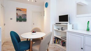 Una habitación con una mesa redonda, dos sillas, una estantería, un televisor y un reloj en la pared.