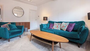 Una sala de estar con dos sofás color turquesa, una mesa de centro de madera, un espejo redondo y una lámpara.