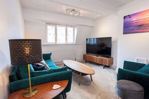 A modern living room with a sofa, a coffee table, a TV, and a painting on the wall. - Cosy 2 Bed Apartment - Close to Leeds Centre (Leeds)