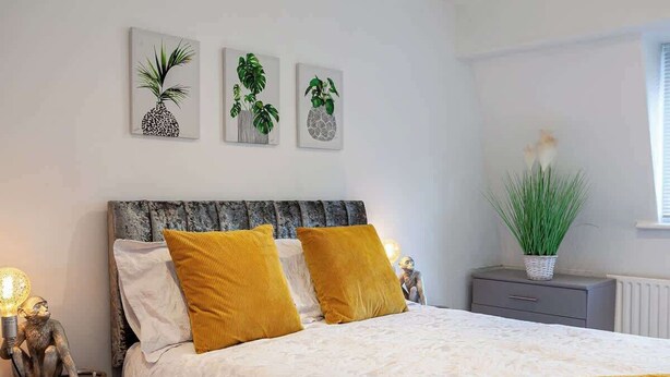 Un dormitorio con cama, dos almohadas, una mesita de noche, lámpara y decoración en la pared.