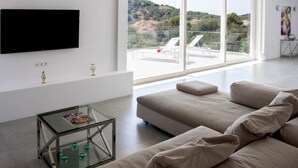 Ein modernes Wohnzimmer mit großem Fenster, Flachbildfernseher und Glastisch.
