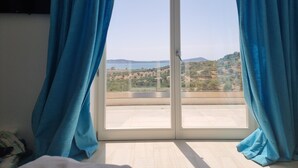 Ein Zimmer mit einer großen Schiebetür und einem Balkon. Es gibt ein Bett mit weißem Kopfteil und einem blauen Vorhang.