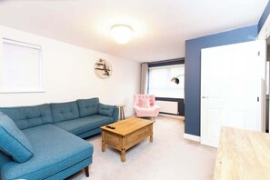 A living room with a blue sofa, a wooden coffee table, a pink chair, and a white door.