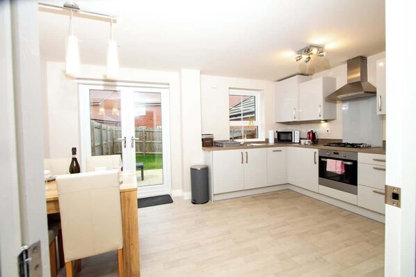 A modern kitchen with white cabinets, a dining area with a table and chairs, and a view of the outdoors.
