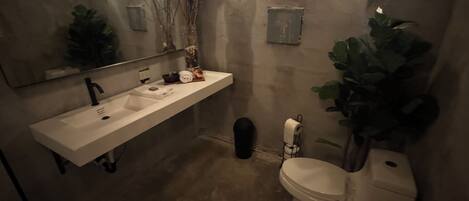 Ein Badezimmer mit weißem Waschbecken, einem Spiegel, einer Toilette und einer Pflanze.