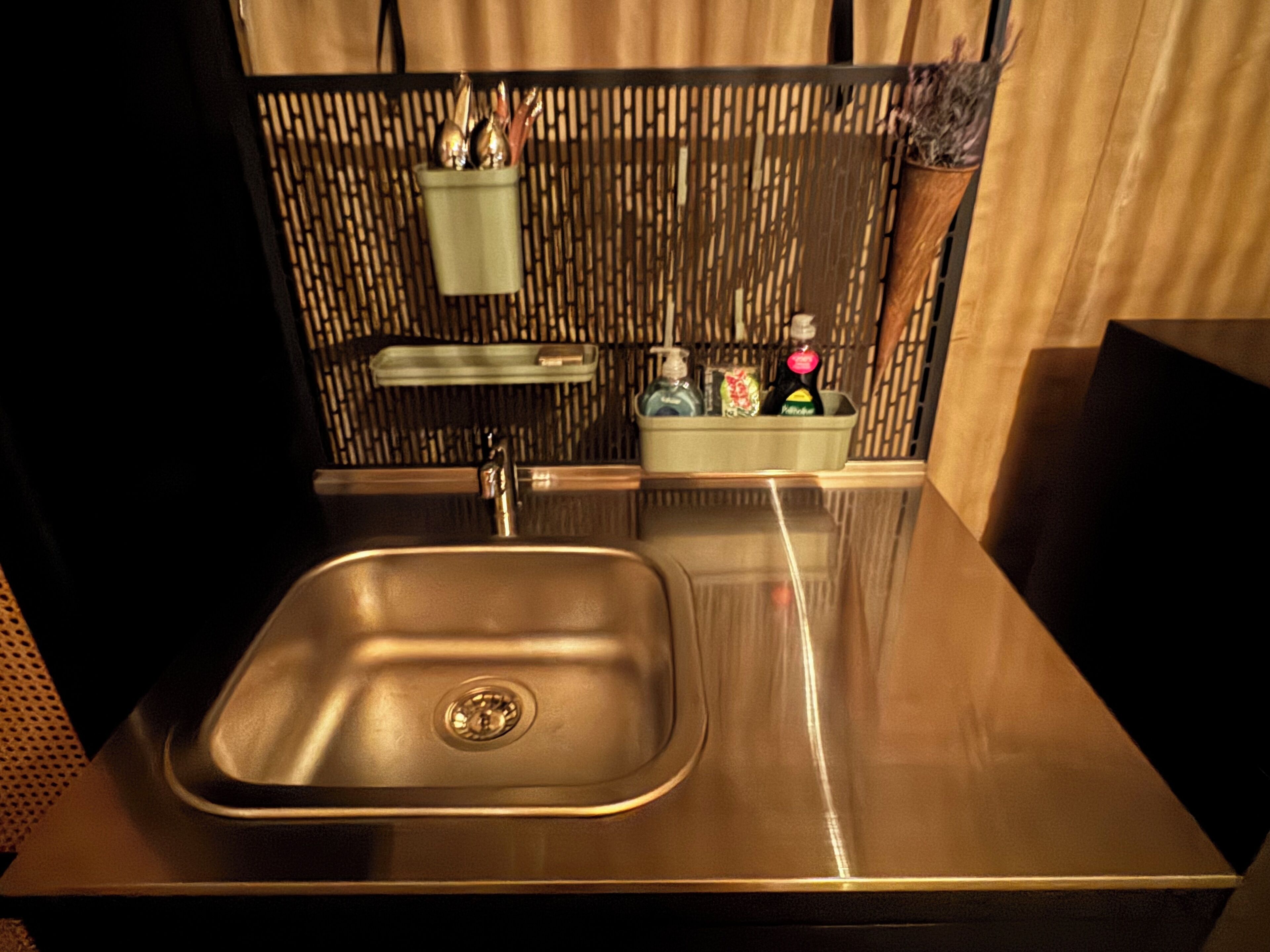 Una cocina moderna con un lavamanos de acero inoxidable, un separador de bambú y un pequeño espacio de almacenamiento con artículos de aseo.