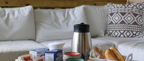A breakfast tray with milk cartons, juice, fruits, and bread on a table in a room with a sofa and patterned cushions.