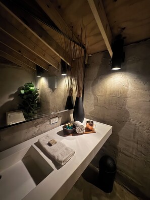 A modern bathroom with a white sink, a mirror, a towel, a cup, and decorative vases. - Jardin al Bosque (San Juan)