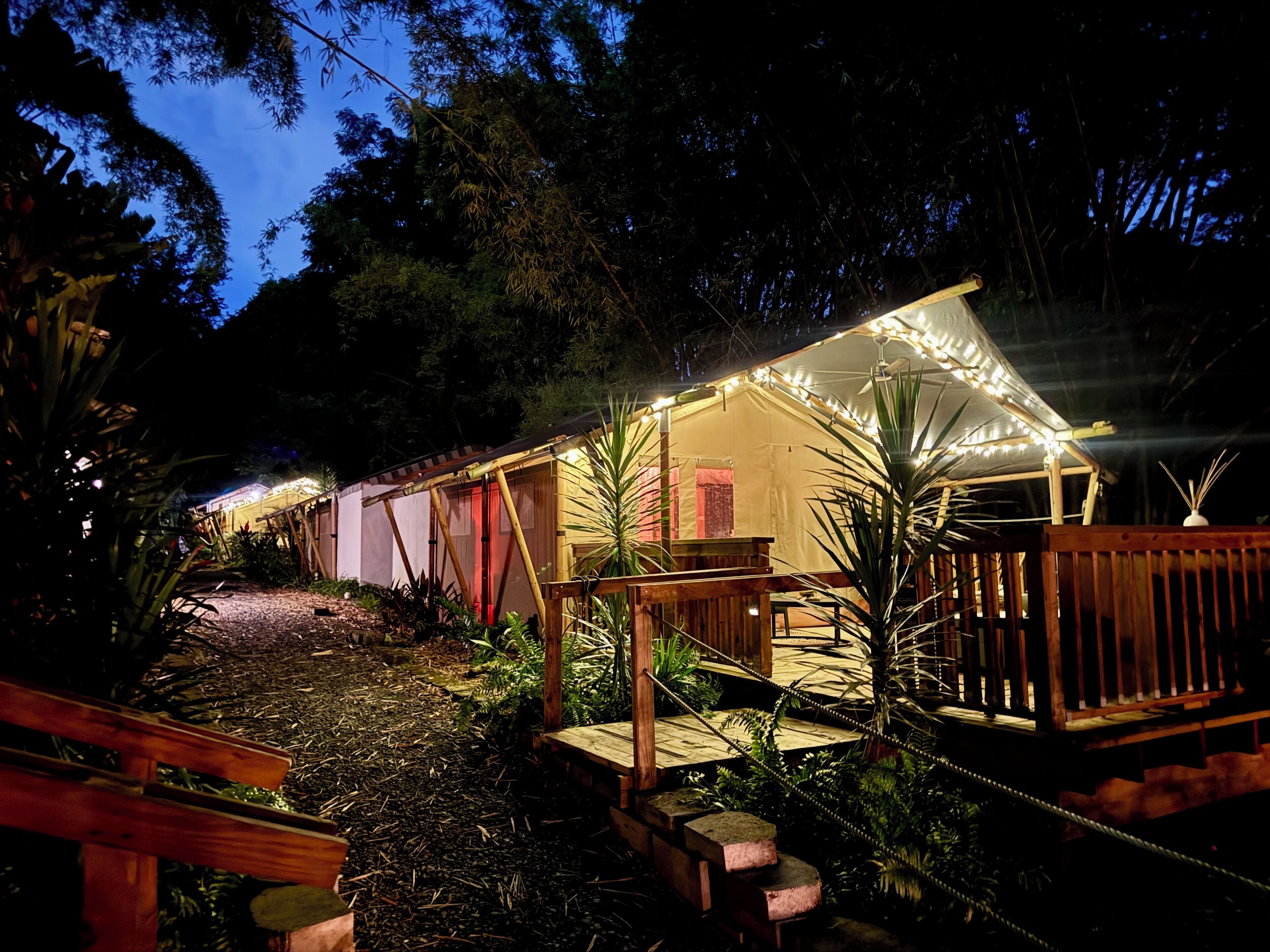 A well-lit outdoor area with a wooden deck, a small bridge, and a tent-like structure with string lights.