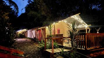 A well-lit outdoor area with a wooden deck, a small bridge, and a tent-like structure with string lights.