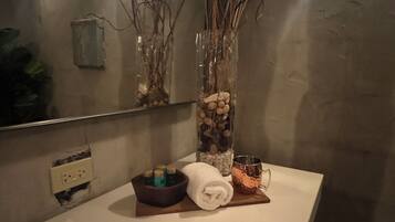 A bathroom with a white countertop, a mirror, a vase with branches and stones, a towel, a copper mug, and a small soap dish.