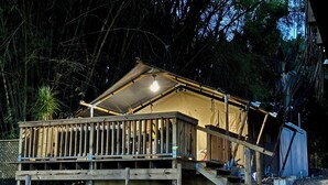 Een houten terras met een balustrade, een overdekt gedeelte met een lamp, en een klein gebouwtje met een dak.