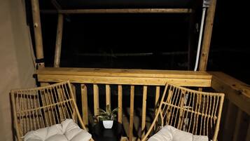 A covered outdoor seating area with two wicker chairs and a small table, under a wooden structure.