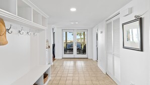 Un pasillo con paredes blancas, suelo de baldosas y una puerta que da a un patio exterior con mobiliario.